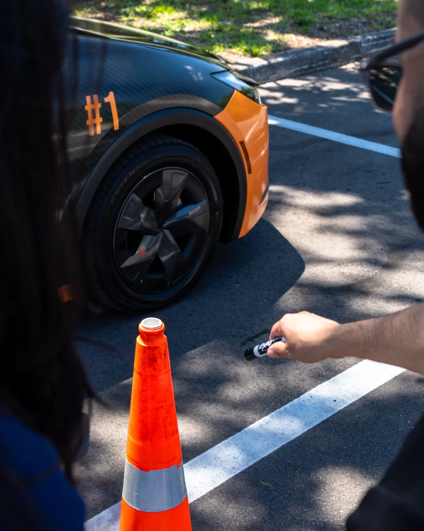 Orange traffic cone on a parking lot line next to the orange and black wrapped lesson car