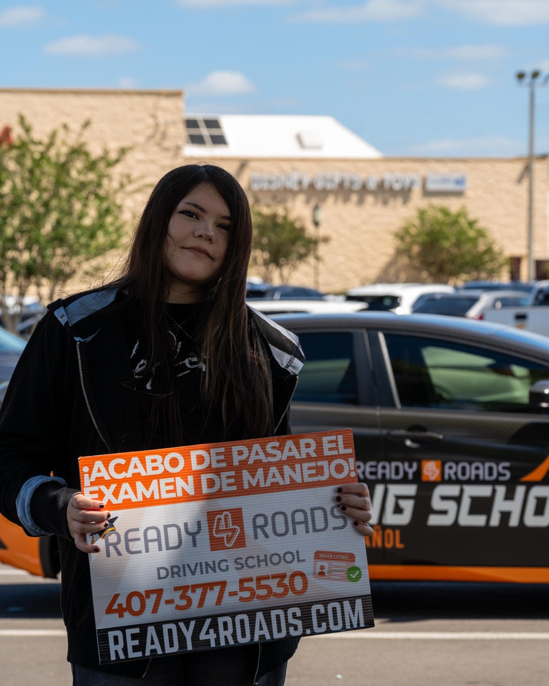 DMV road test prep student of Ready 4 Roads holding pass sign in Kissimmee FL parking lot